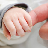 hand of baby holding on to finger of parent