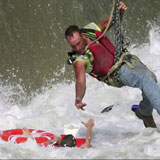 Rescuer being lowered from helicopter reaching down to grab person from turbulent water